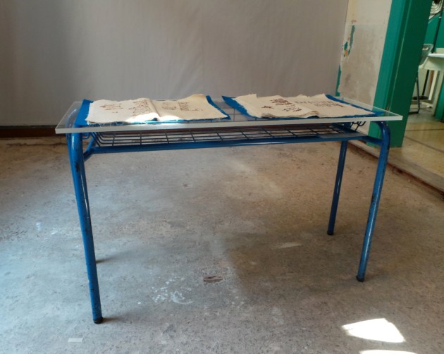 Ονόματα μαθητών, 2012-15, σιδερένια βάση θρανίου, επιφάνεια πλεξιγκλάς και 2 τετράδια από ύφασμα, κεντημένα στο χέρι με βαμβακερές κλωστές σε ακατέργαστο βαμβακερό ύφασμα, 32x25 και 42x26 εκατοστά, εγκατασταση στο bhive 